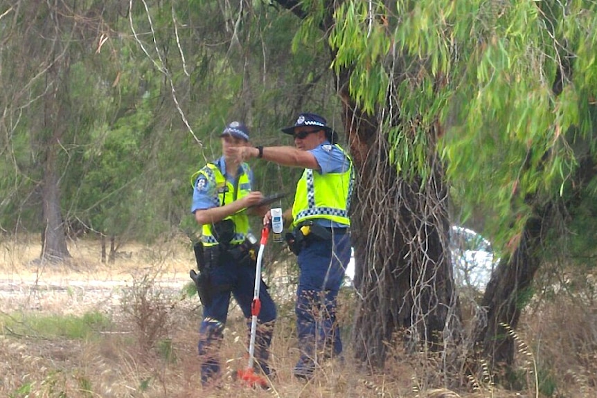 Two police officers in high-viz vests stand on a bushy roadside next to the Forrest Highway.