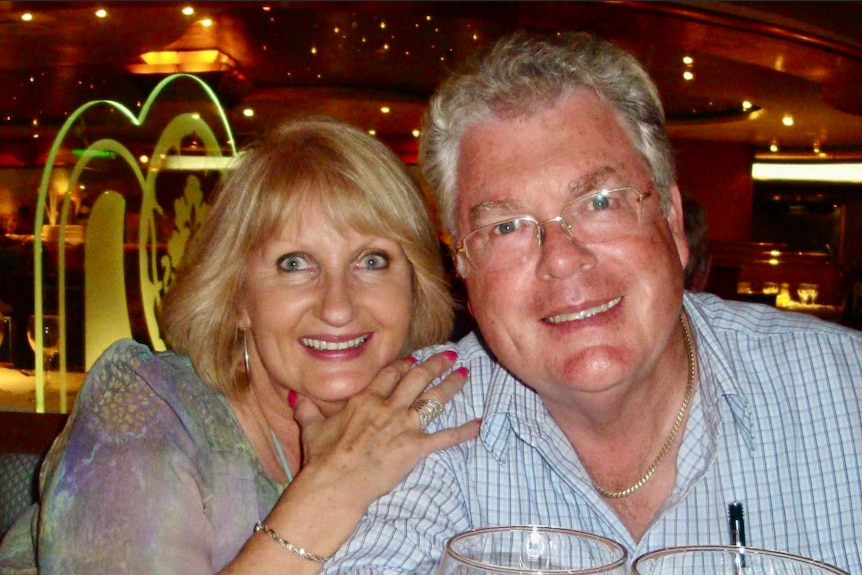 A senior man and woman smile, with drinks on their table.