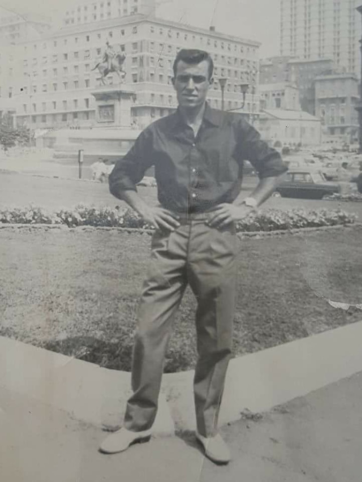 a black and white photo of a man in a long shirt standing in a European square