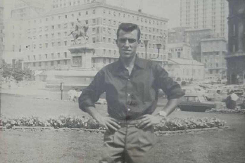 a black and white photo of a man in a long shirt standing in a European square