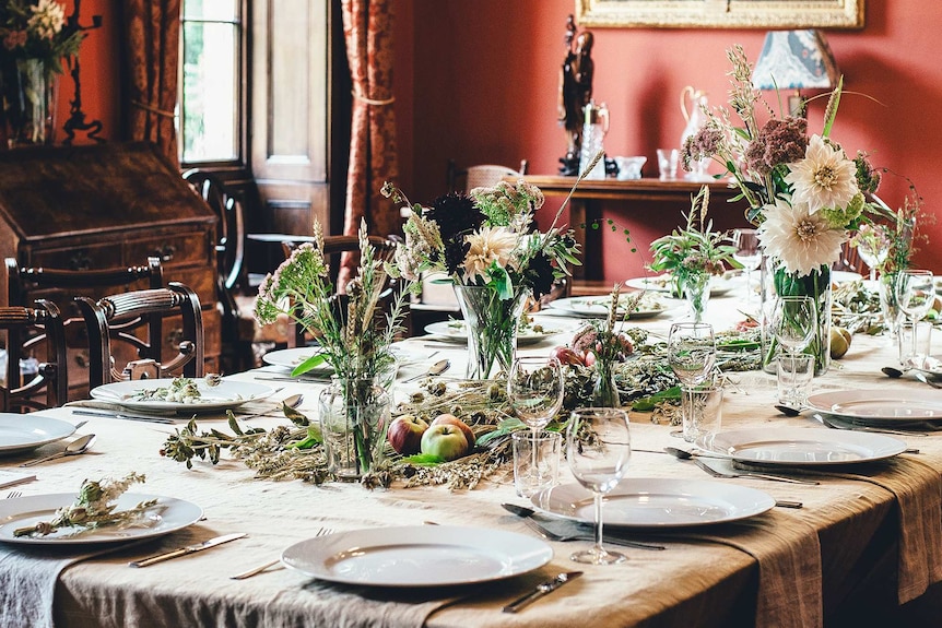 Set dining table with flowers and centrepiece in a large room to depict a story about the decline of dinner parties.