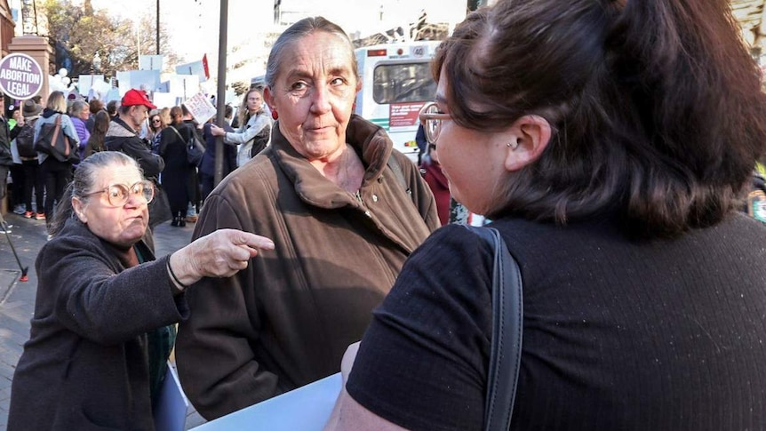 An older lady points her finger at a younger woman as another woman stands between them.