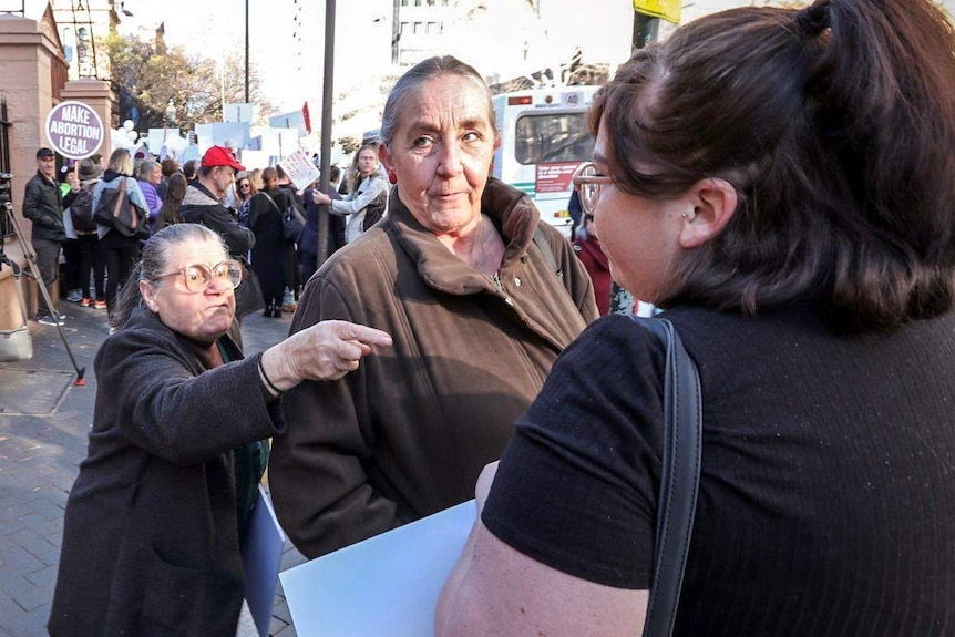 An older lady points her finger at a younger woman as another woman stands between them.