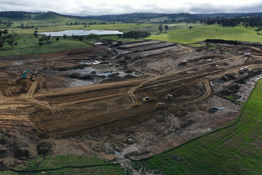Aerial photograph of a dam under construction, surrounded by green paddocks
