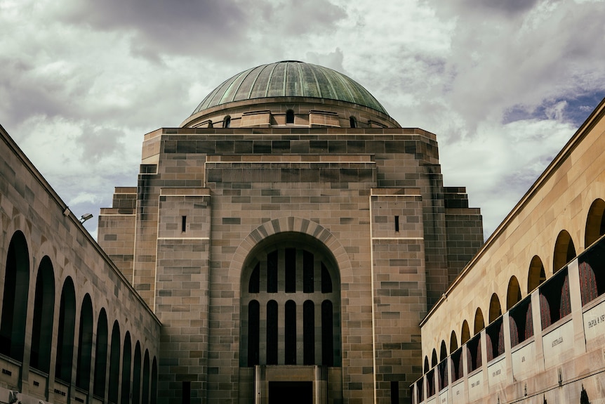 A grand sandstone dome with arches on either side, under a cloudy sky