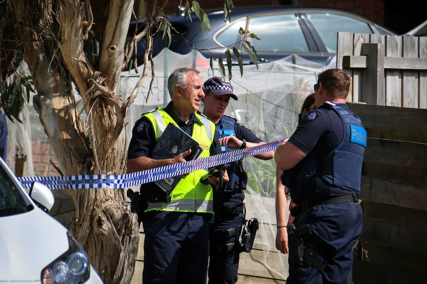 Several police officers stand by a tree near police tape.