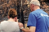 Two people cry outside a burnt-out house