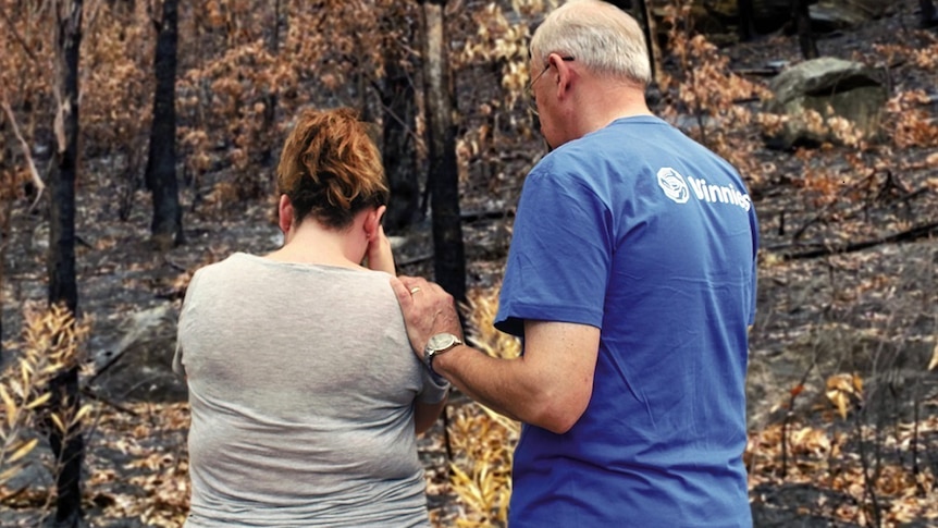 Two people cry outside a burnt-out house