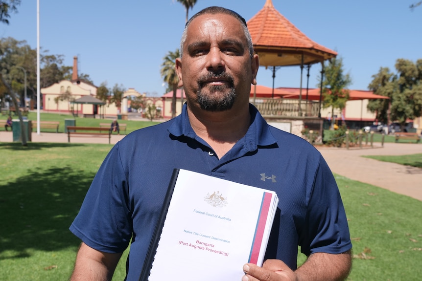 An Indigenous man stands outside holding a document.