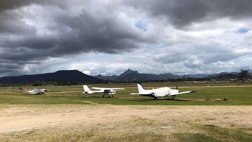 planes on a rural airport with clouds and mountain in background