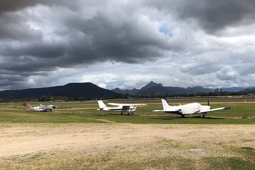 planes on a rural airport with clouds and mountain in background