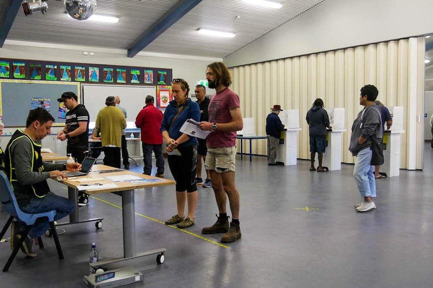 Locals in Alice Springs line up to place their votes in the 2020 NT Election. People inside a building prepare to vote.