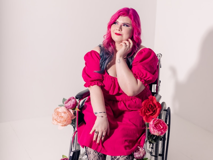 A woman with bright pink hair and wearing a pink dress sitting in a wheelchair