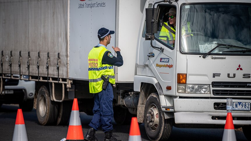 A man in uniform speaks to a driver who is sitting in a large truck