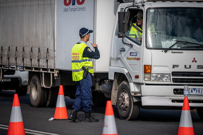 A man in uniform speaks to a driver who is sitting in a large truck