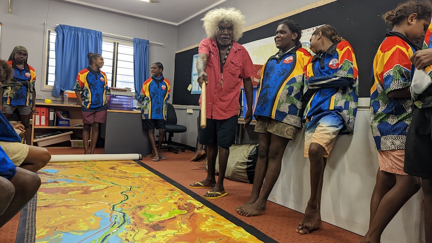 A group of Indigenous people gather around a large map rolled out on the floor showing a river.