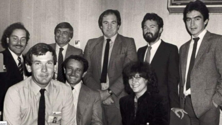 Black and white photo of Barrie Cassidy standing with seven colleagues.