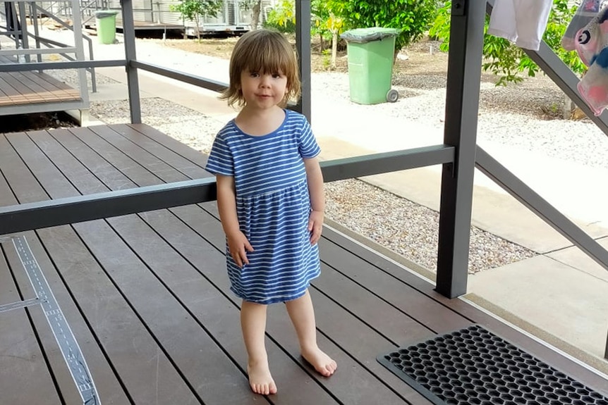 A toddler in a blue dress climbs on the stairs of a balcony