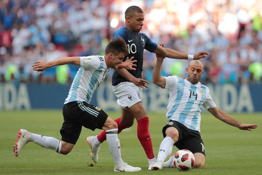 Kylian Mbappe runs between two Argentina players who both attempt to slide tackle him