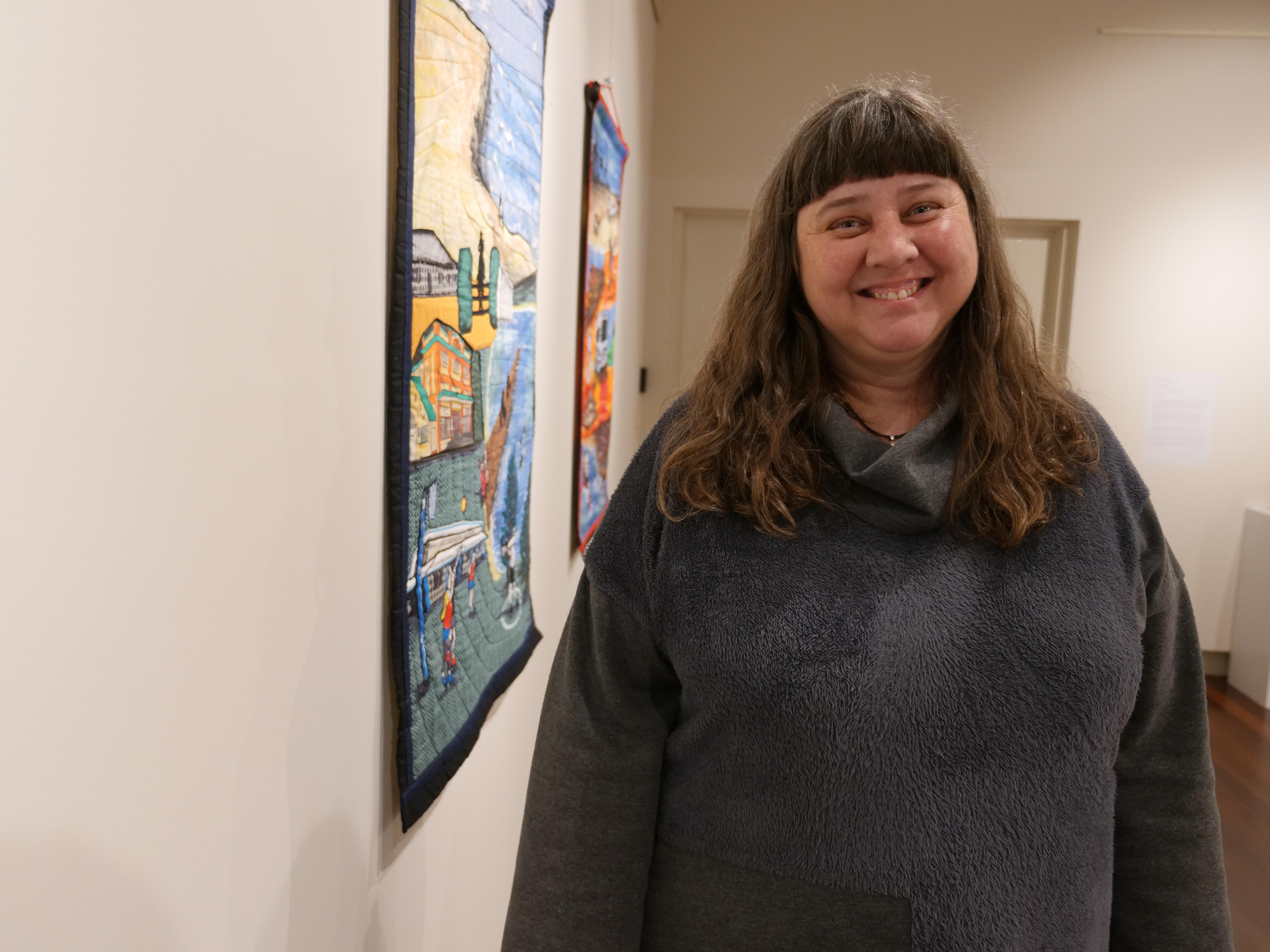 Woman stands beside a painting and smiles at the camera 