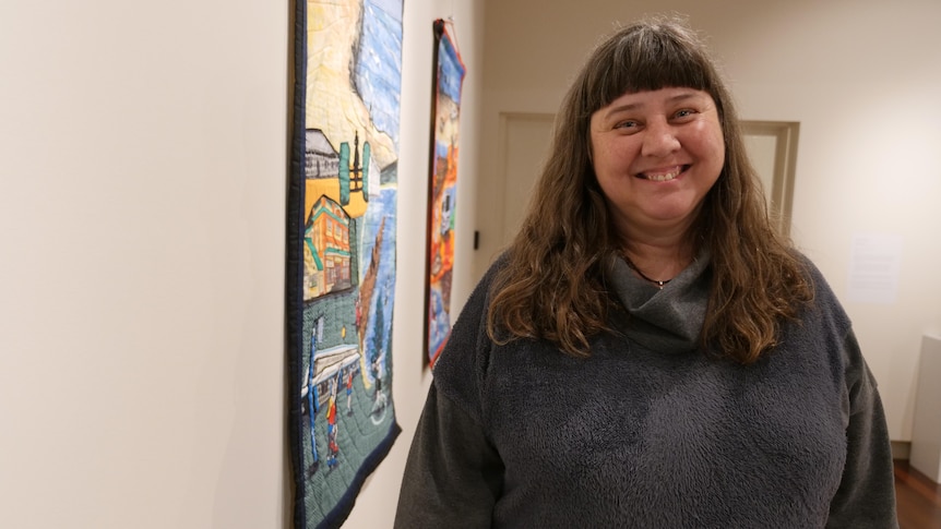 Woman stands beside a painting and smiles at the camera 