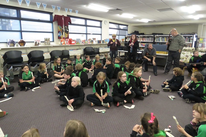 A class of young children sit on the floor of a classroom with recorders.