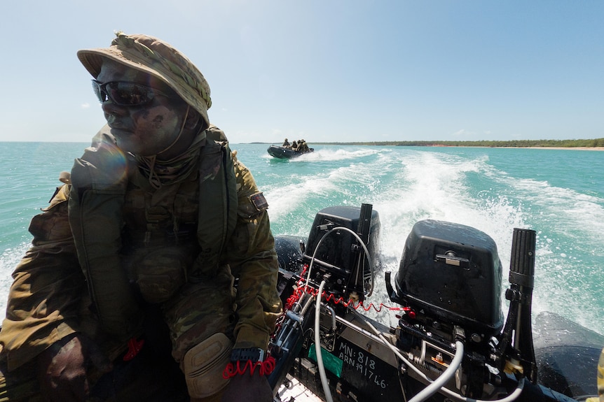 an aboriginal man in army uniform driving a boat on the ocean
