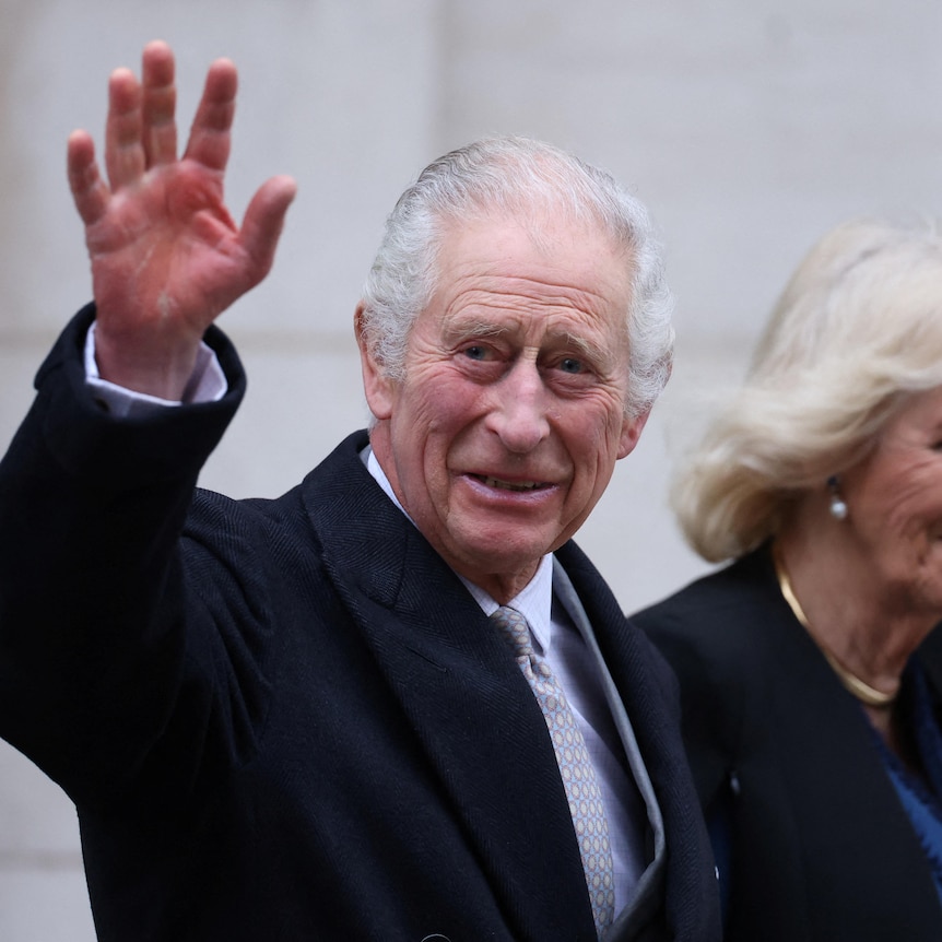 King Charles waves as he walks alongside Queen Camilla 