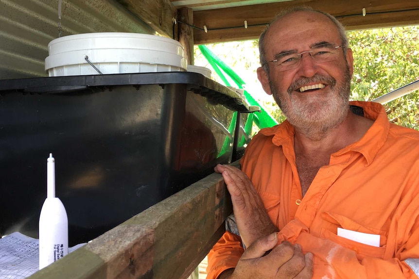 Man in orange shirt stands beside black tank