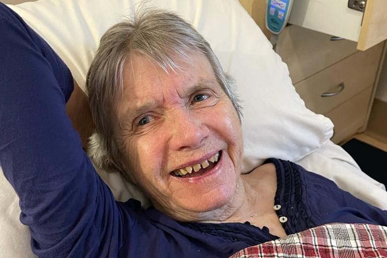 an elderly woman lying in a bed looking at the camera and smiling