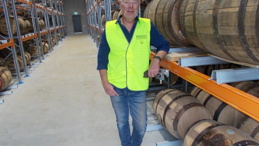 A man in a yellow vest standing next to a number of barrels of whiskey at a new distillery in southern Tasmania