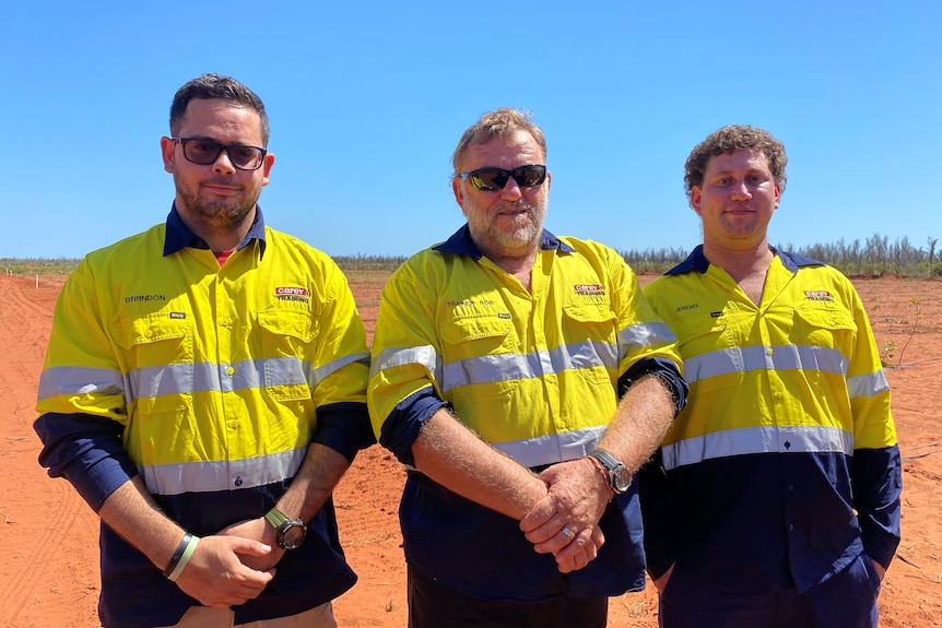 Three men standing shoulder to shoulder, wearing yellow and navy hi-vis shirts. First two are wearing sunglasses