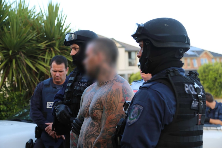 a tattooed, shirtless man with several police officers.
