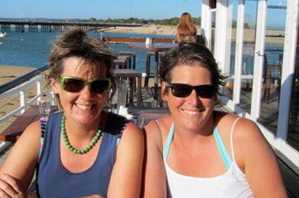 Two women pose for a photo while seated at an outdoor cafe