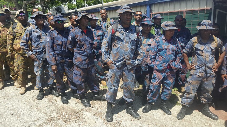 PNG police and soldiers wearing fatigues line up in a row as they wait to board a flight