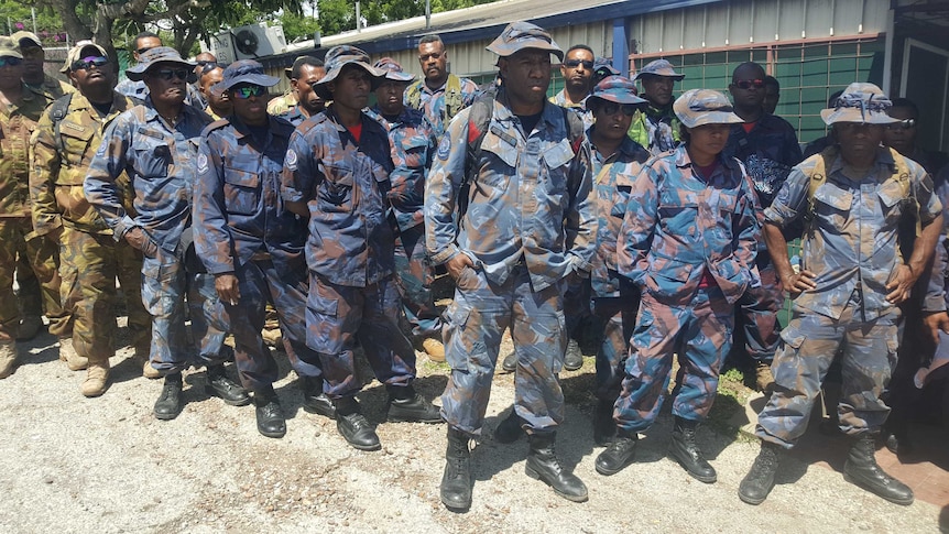 PNG police and soldiers wearing fatigues line up in a row as they wait to board a flight