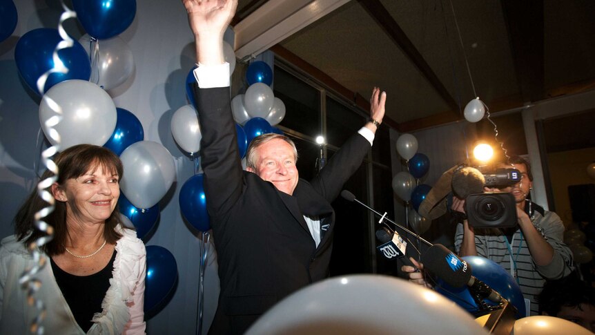 Liberal leader Colin Barnett stands with his arms aloft next to his wife lyn with blue and white balloons around them.