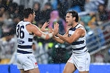 Two AFL players clap hands and celebrate in the rain