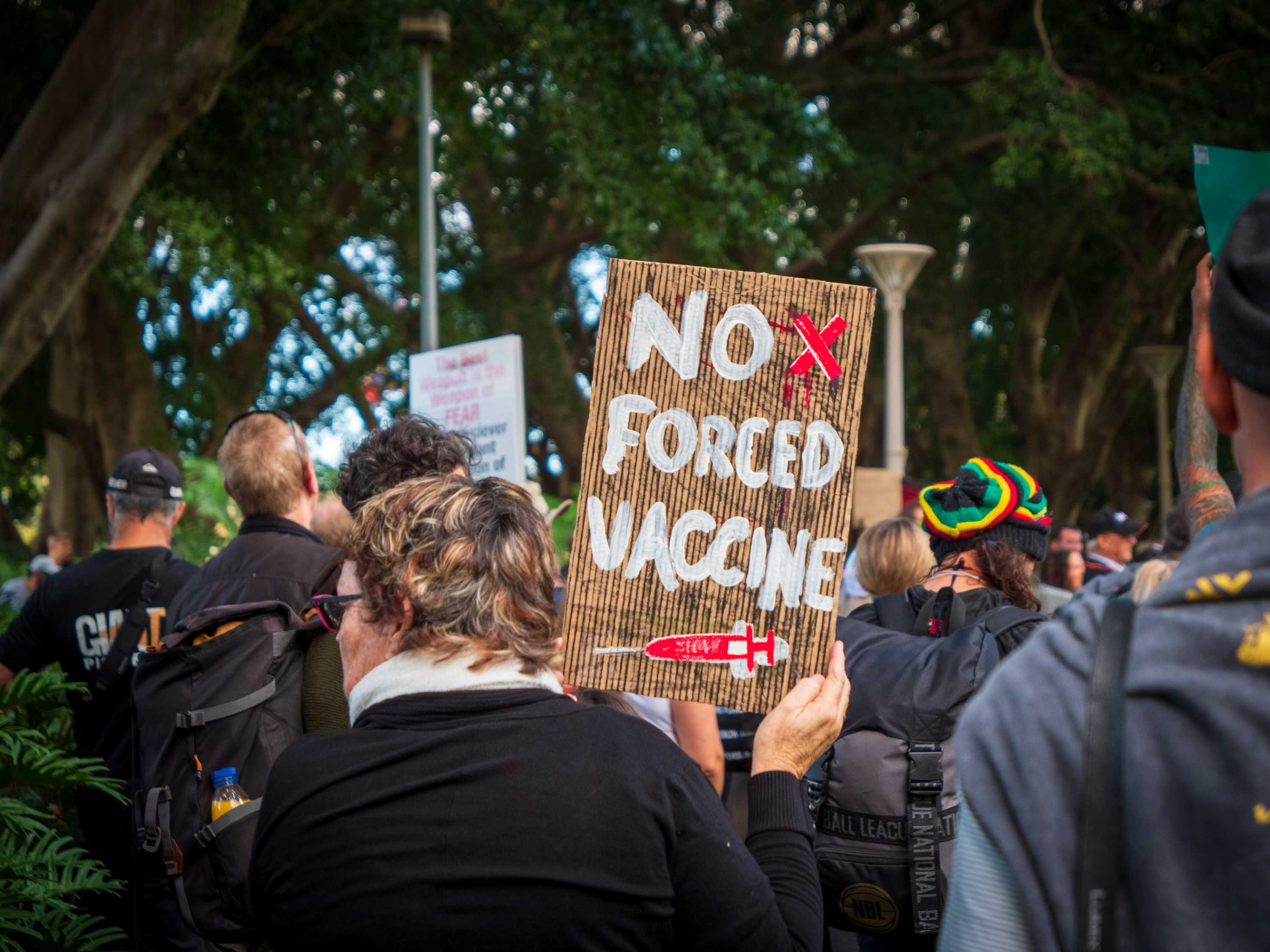 A woman holds a sign at a protest that says "no forced vaccine".