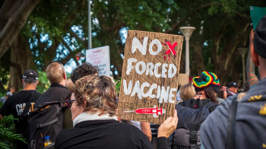 A woman holds a sign at a protest that says "no forced vaccine".