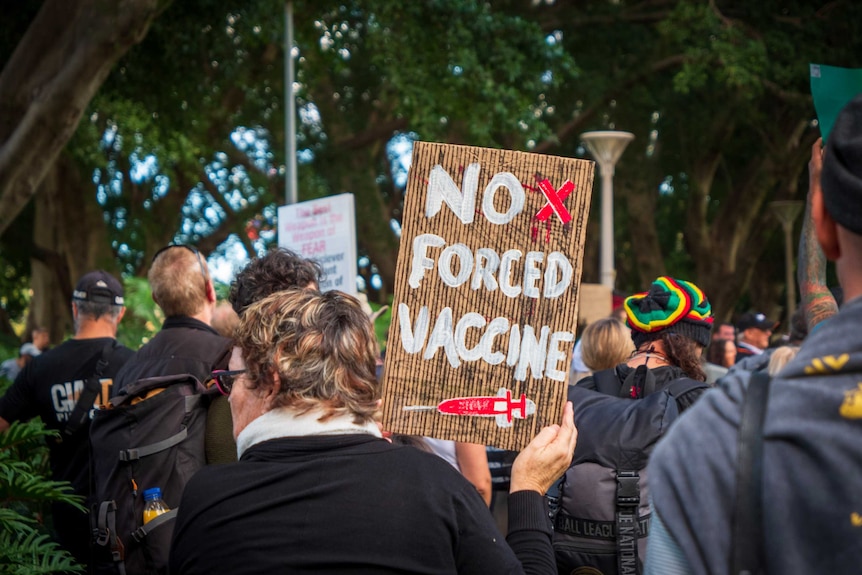 A woman holds a sign at a protest that says "no forced vaccine".
