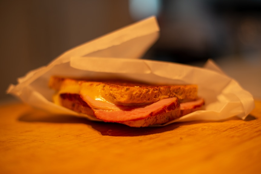 A ham and cheese toasted sandwich wrapped in baking paper.