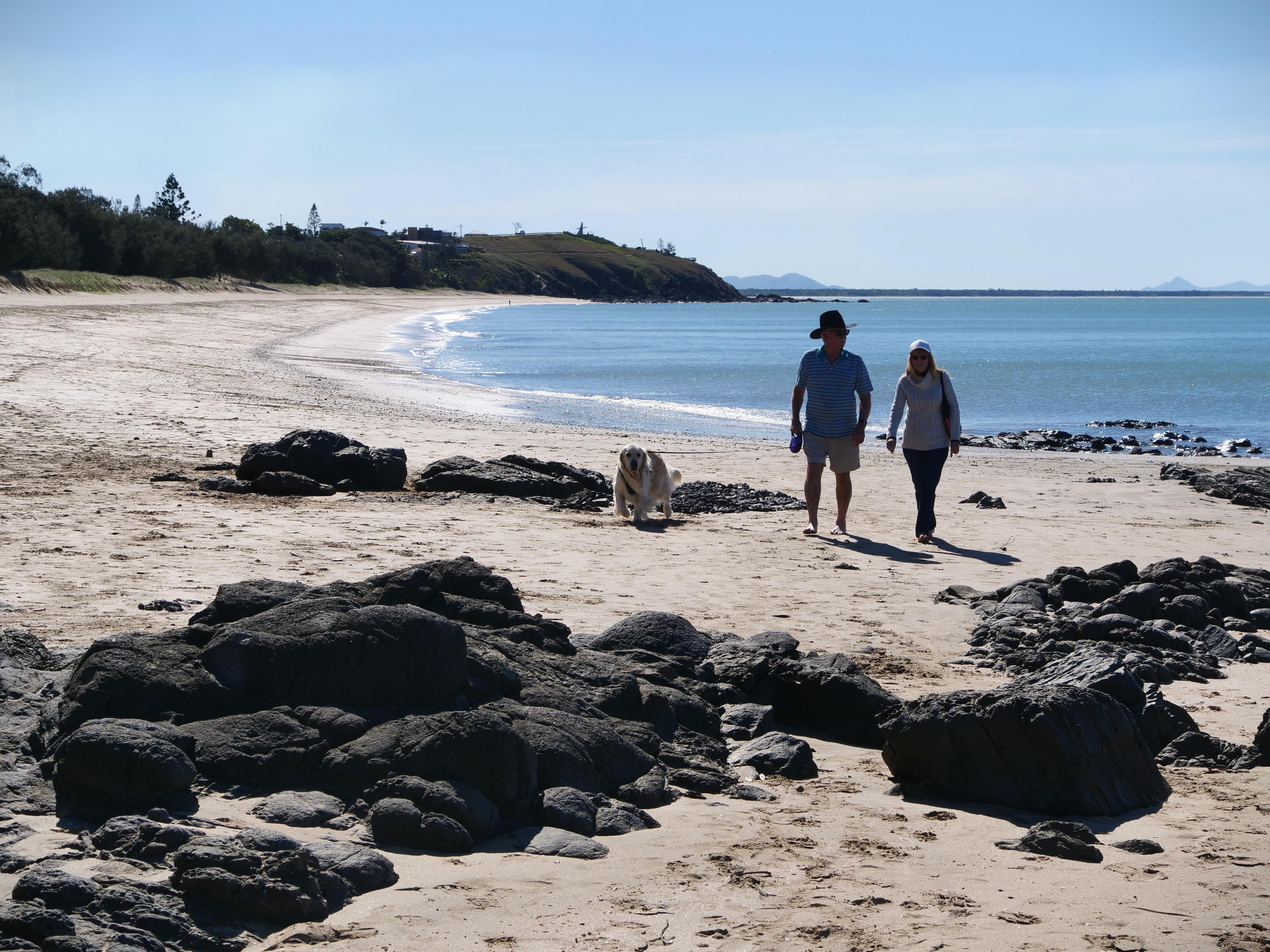 Two people walking on a rocky beach with a golden retriever 