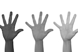 Three hands belonging to people of different nationalities are in the air.