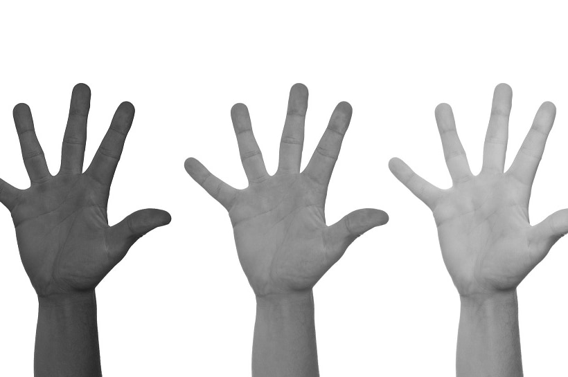 Three hands belonging to people of different nationalities are in the air.