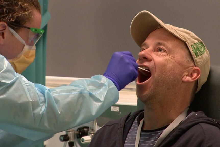 A man wears a cap as a medical professional wearing protective gear swabs his mouth during a test for coronavirus.