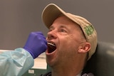 A man wears a cap as a medical professional wearing protective gear swabs his mouth during a test for coronavirus.