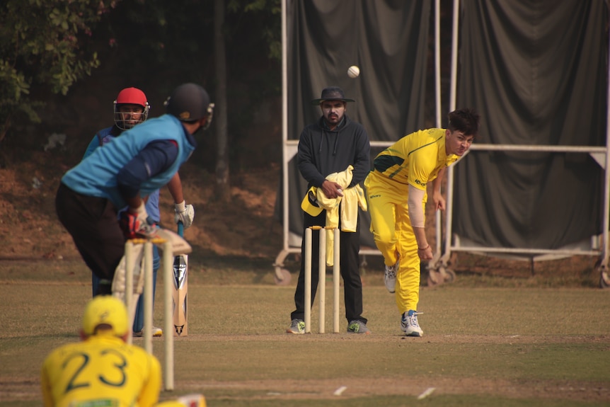 Callum Asbury bowls a ball towards a batsman who is wearing blue cricket kit