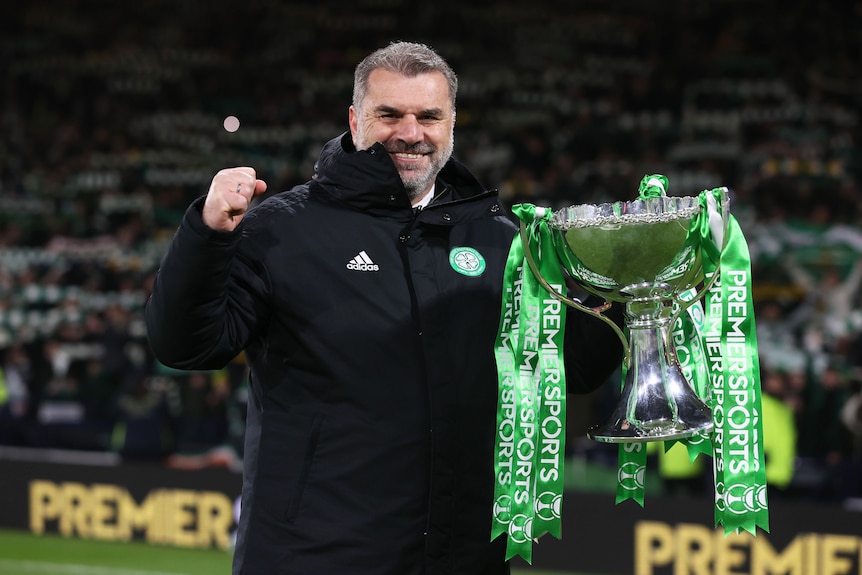 A man in a black jack holds a silver cup with green ribbons.