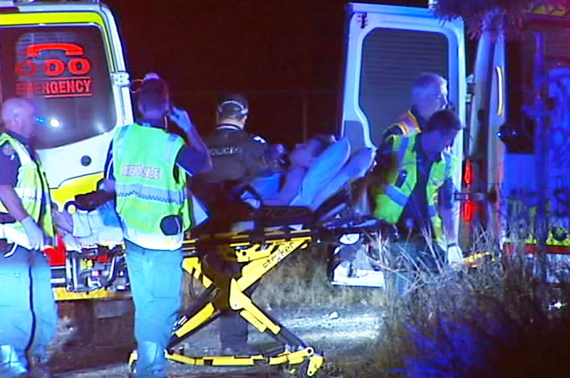 A boy on a stretcher surrounded by police and ambulance officers.